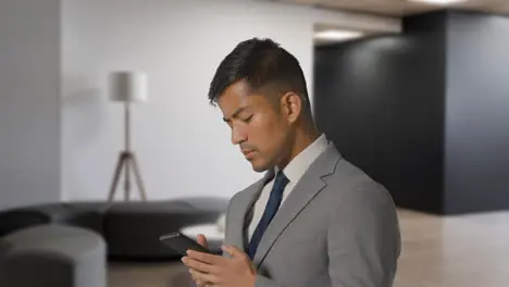 Serious Businessman In Suit Messaging On Mobile Phone In Modern Open Plan Office