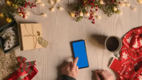 Overhead Shot Of Person Holding Blue Screen Mobile Phone With Christmas Decorations And Wrapping 3