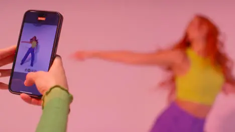 Studio Shot Of Woman Taking Photo Of Friend Dancing On Mobile Phone Against Pink Background 6