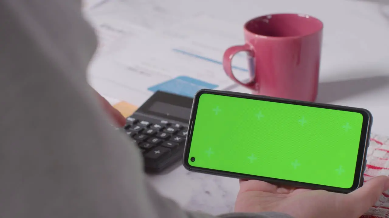 Close Up Of Person Holding Green Screen Mobile Phone Looking Through Bills In Kitchen 2