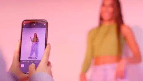 Studio Shot Of Woman Taking Photo Of Friend Dancing On Mobile Phone Against Pink Background 2