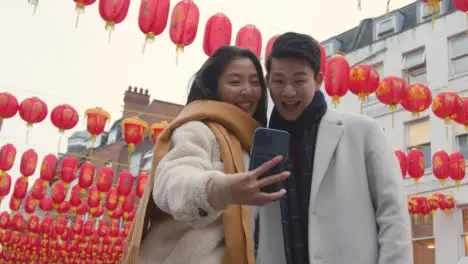 Young Asian Couple On Holiday Posing For Selfie On Mobile Phone In Chinatown London UK