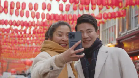 Young Asian Couple On Holiday Posing For Selfie On Mobile Phone In Chinatown London UK 5