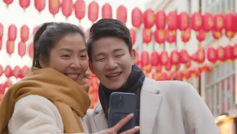 Young Asian Couple On Holiday Posing For Selfie On Mobile Phone In Chinatown London UK 6