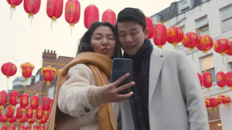 Young Asian Couple On Holiday Posing For Selfie On Mobile Phone In Chinatown London UK 1