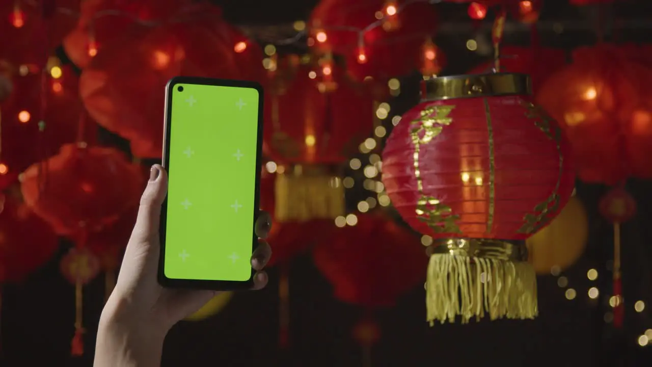 Hand Holding Green Screen Mobile Phone With Chinese Lanterns Hung In Background 2