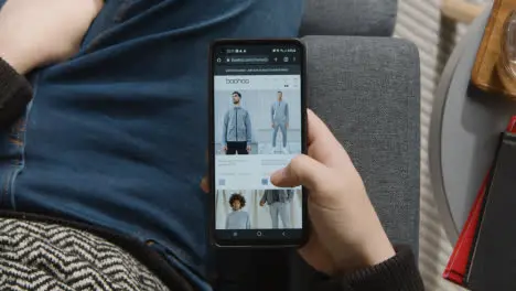 Overhead Shot Of Person At Home Shopping Online Looking At Boohoo Website On Mobile Phone