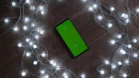 Overhead Shot Of Revolving Green Screen Mobile Phone With Christmas Decorations And Lights