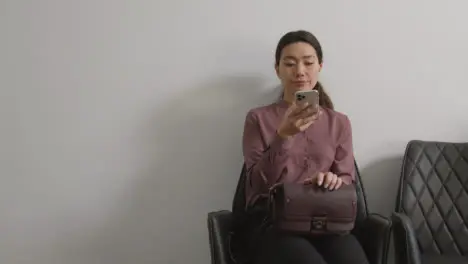 Female Candidate Wearing Suit In Office Waiting For Job Interview Looking At Mobile Phone