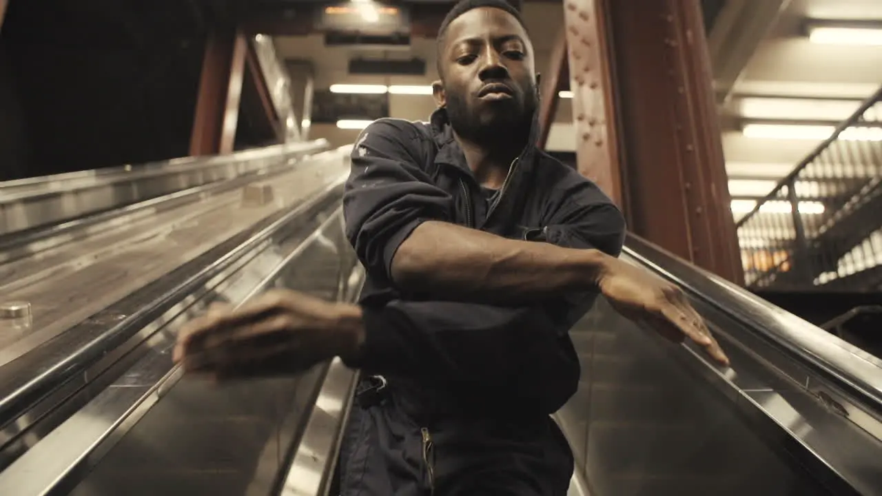 Janitor dancer twists arms as escalator takes him up medium closeup