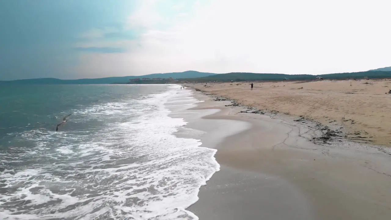 Drone flying straight ahead parallel the seashore in cloudy day with seagulls in front Sozopol Bulgaria