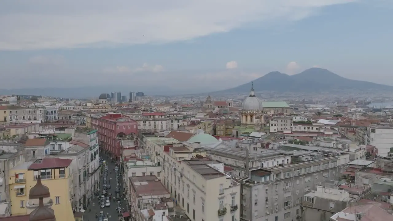 Aerial video flying over buildings in Naples Italy and focusing on the spire of a church with Mount Vesuvius in the background