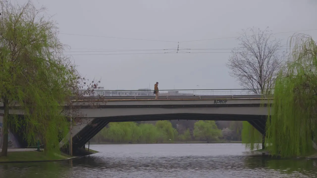 Static shoot of person passing left to right on a bridge over a body of water in the city with traffic in the background