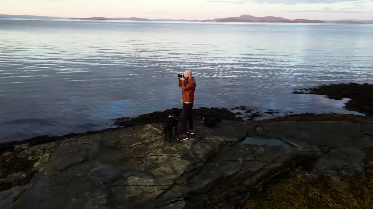 Aerial footage of a man standing at the shore and taking pictures with a camera