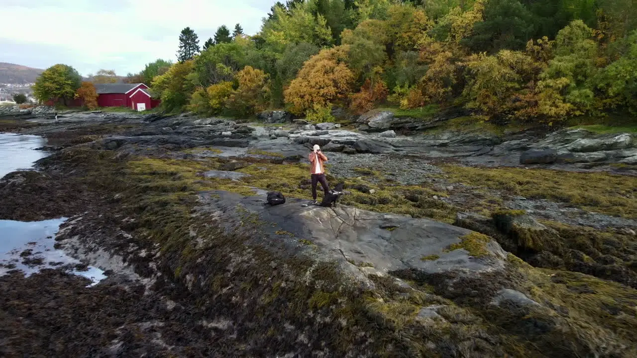 Aerial footage closing in on a man standing at the shore and taking pictures with a camera