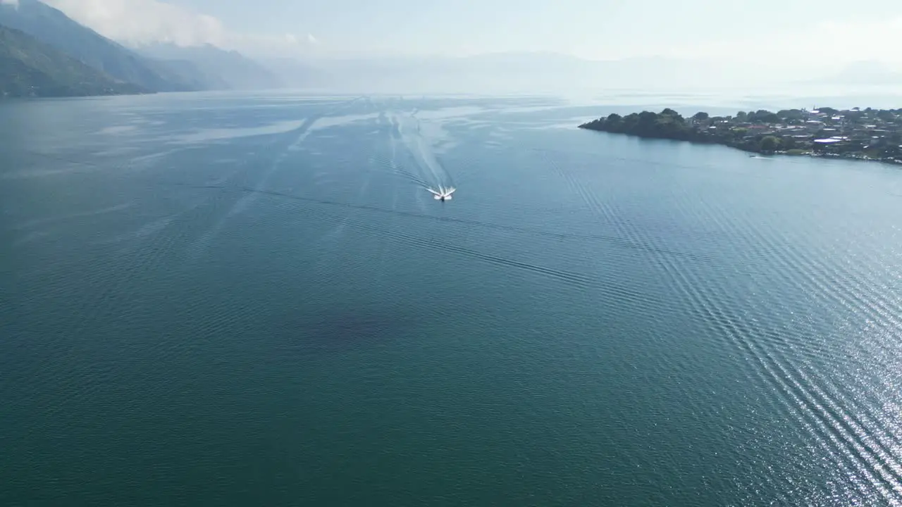 Drone view in Guatemala flying over a boat on a blue lake with green mountains on the side on a sunny day in Atitlan