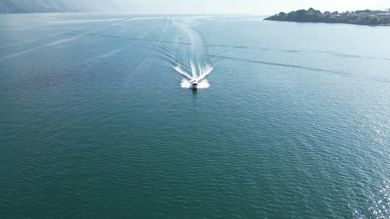 Drone view in Guatemala flying close over a boat on a blue lake with green mountains on the side on a sunny day in Atitlan