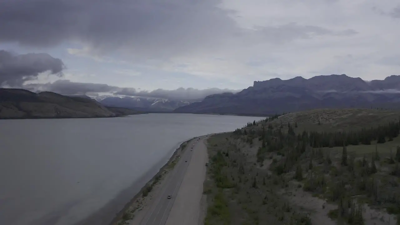 Mountains lake roadside highway light traffic with partly cloudy day and sunlight behind clouds