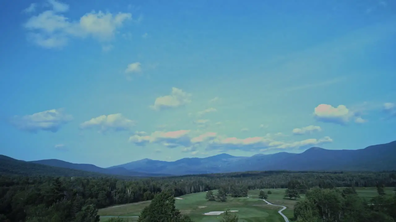 The white mountain range in New Hampshire sits under a blue cloudy sky beyond forest which surrounds a gold course