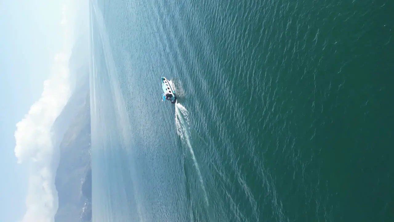 Drone portrait view in Guatemala circling around a boat over a blue lake surrounded by green mountains and volcanos on a sunny day in Atitlan