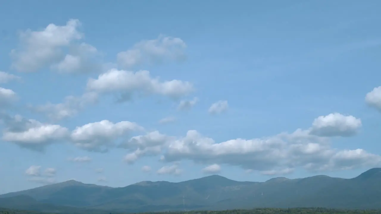 A tilt reveal of a blue cloudy sky to the white mountains of New Hampshire to a green forest beyond a golf course