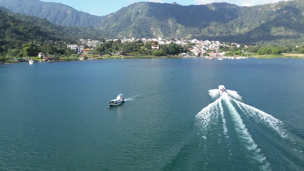 Drone view in Guatemala flying over boats on a blue lake with green mountains and volcanos on a sunny day in Atitlan