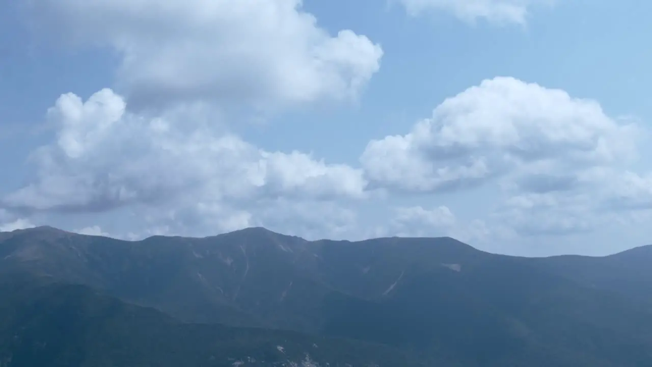 A hazy mountain sits under a cloudy blue sky as the camera tilts down