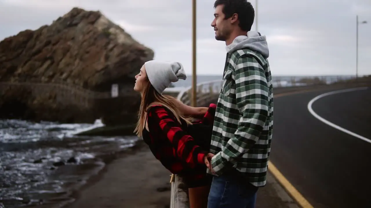 Woman And Man Gazes At Ocean Young Couple Shown From The Side Look Out Over An Ocean In Front Of The Hills Talking Embracing