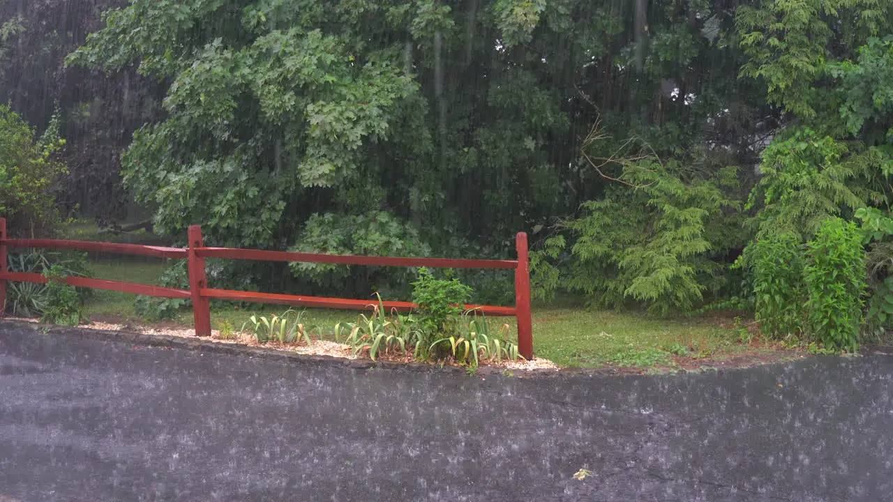 A heavy rain falling on the driveway outside during a thunderstorm with a spilt rail fence in the background