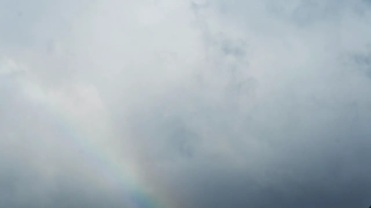 Time lapse of a rainbow appearing and becoming more vivid with clouds moving behind it