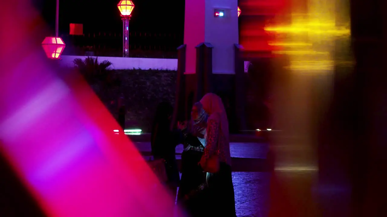 Muslim women taking selfies around multicolored flashing lights at night