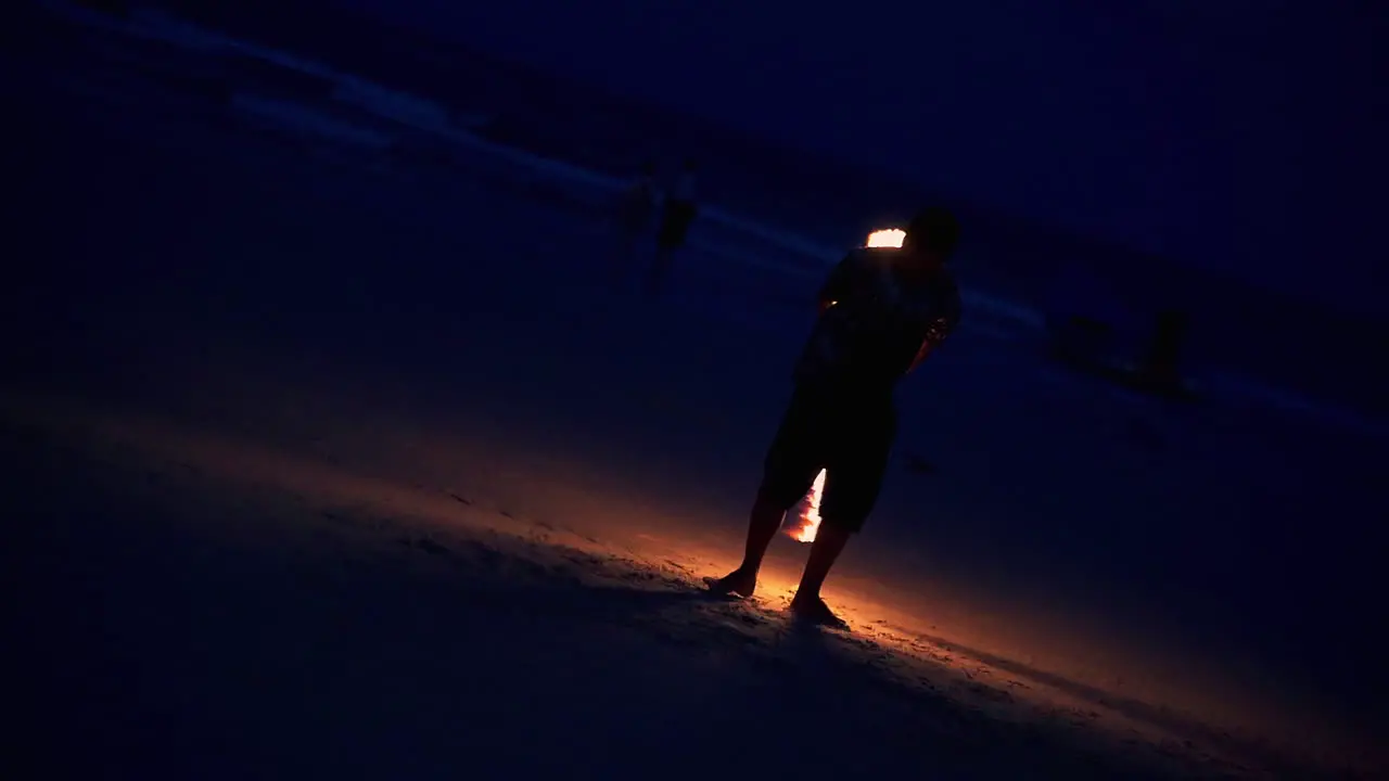 Performer skillfully spinning flaming stick at night beach fire show