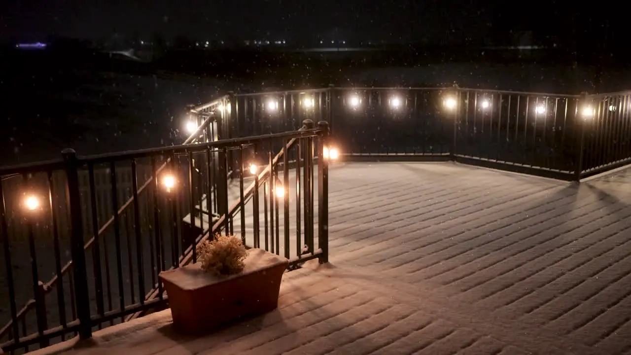 Fresh gently snow falling on a peaceful night static view of a lit patio or deck