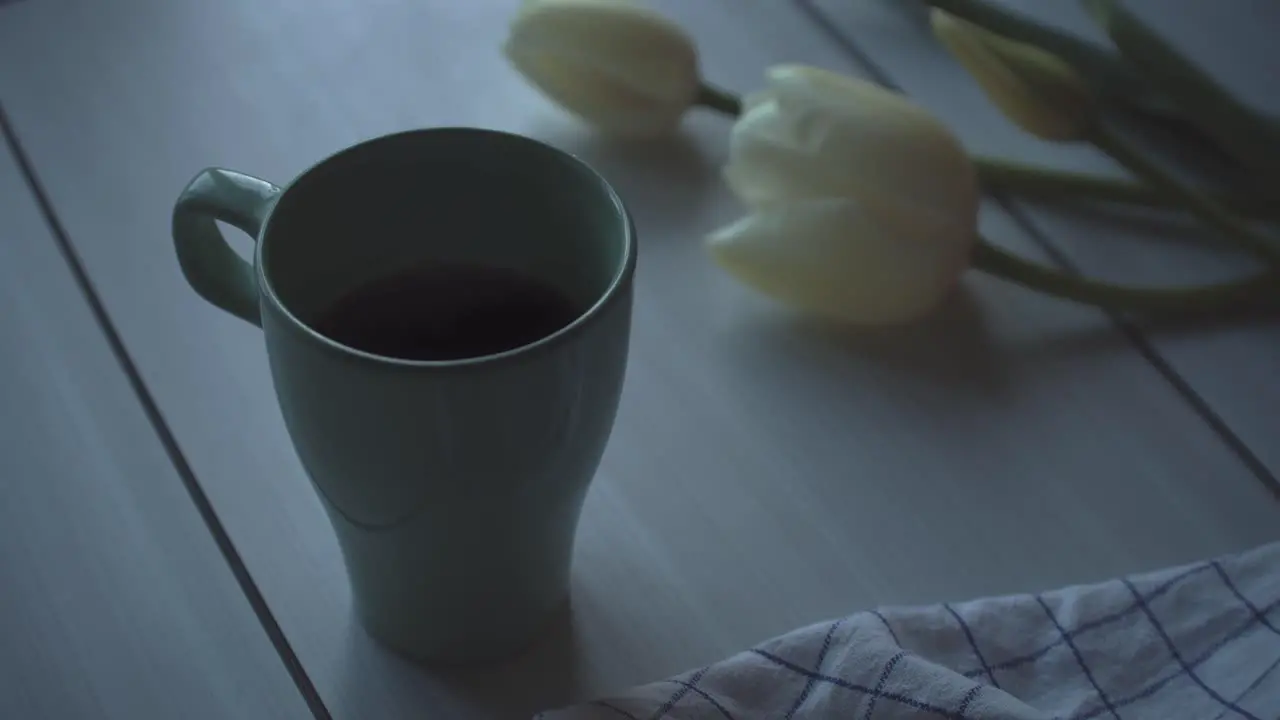 Tea cup on wooden table with tulips and a sheet resting on it