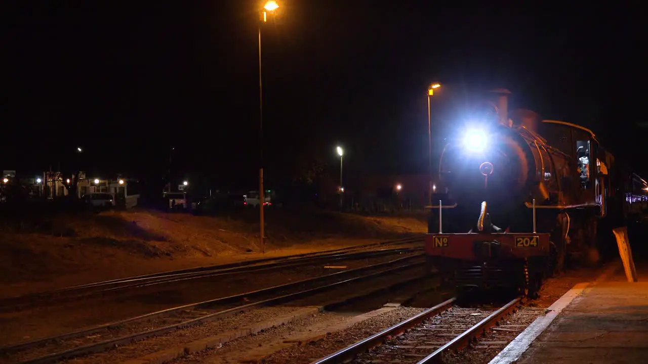 An old steam train pulls into a station at night in Zimbawbwe Africa with wealthy tourists on board