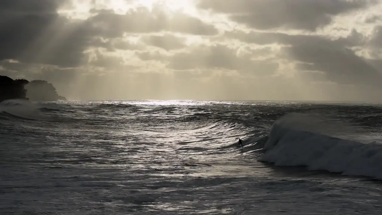 Unrecognisable lone surfer riding wave from right to left of screen during stormy sunrise at Bronte Beach Sydney