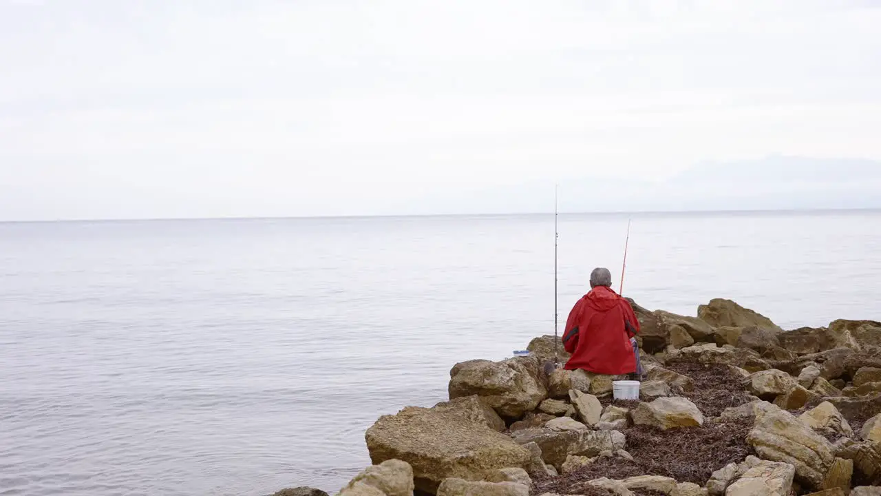 A fishman sits on a rock and looks out to sea