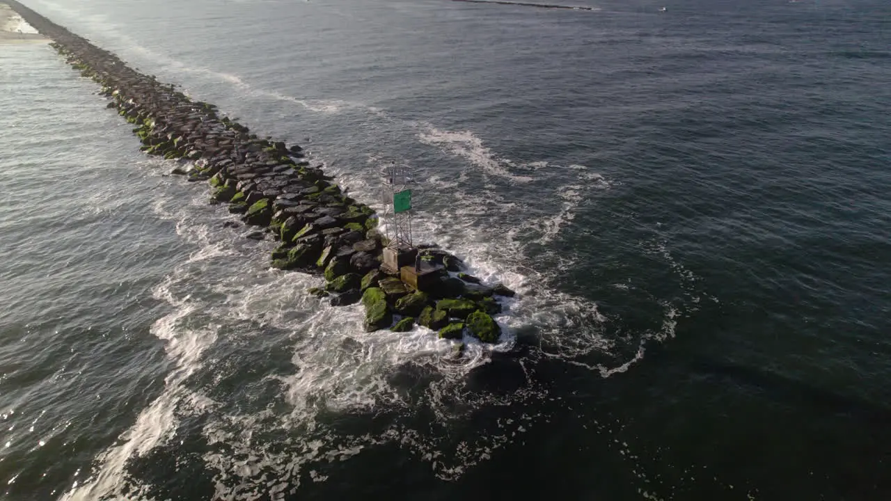 Man fishing casting line into ocean from Jetty Aerial Drone shot near channel marker bouy on rocks