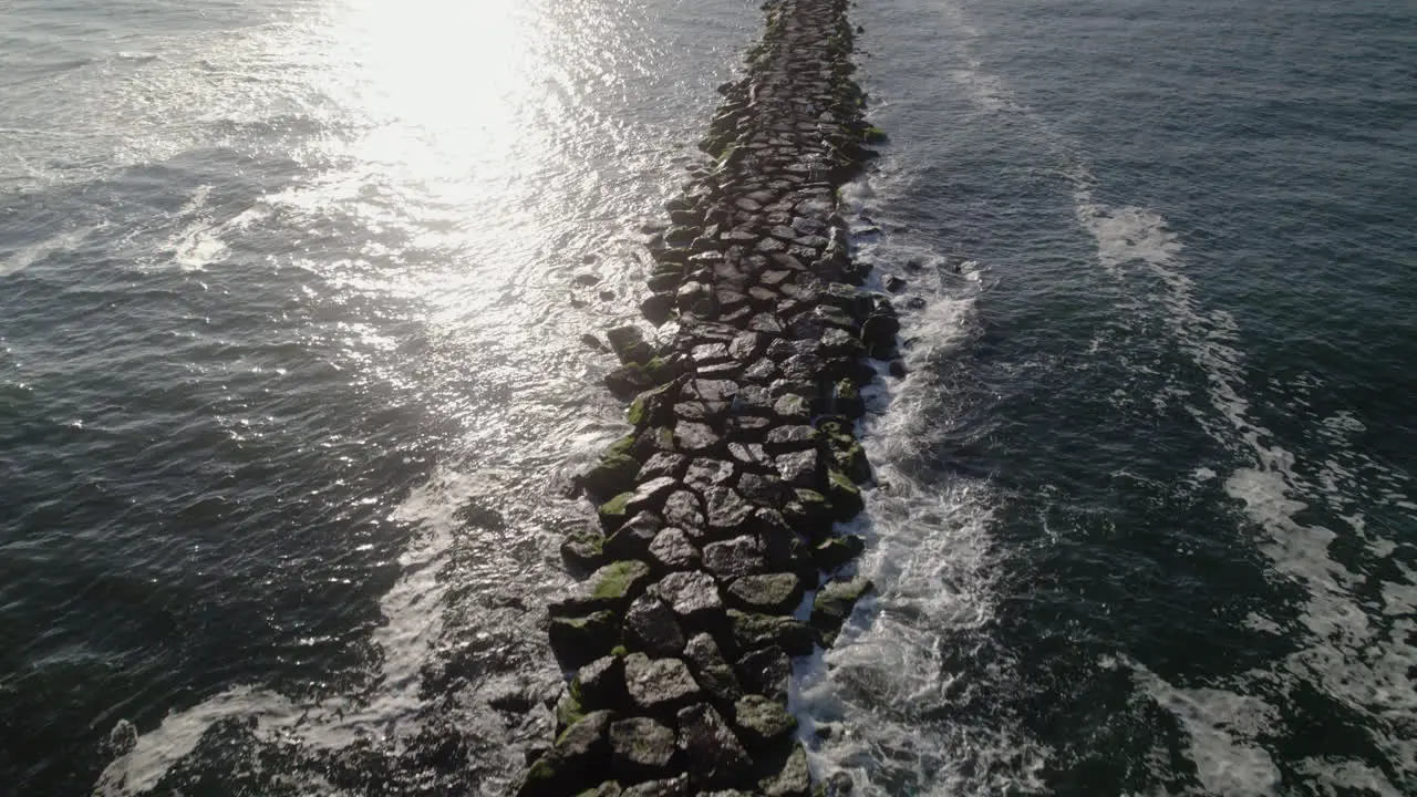 Aerial drone fly over channel marker and rocky jetty with lens flare