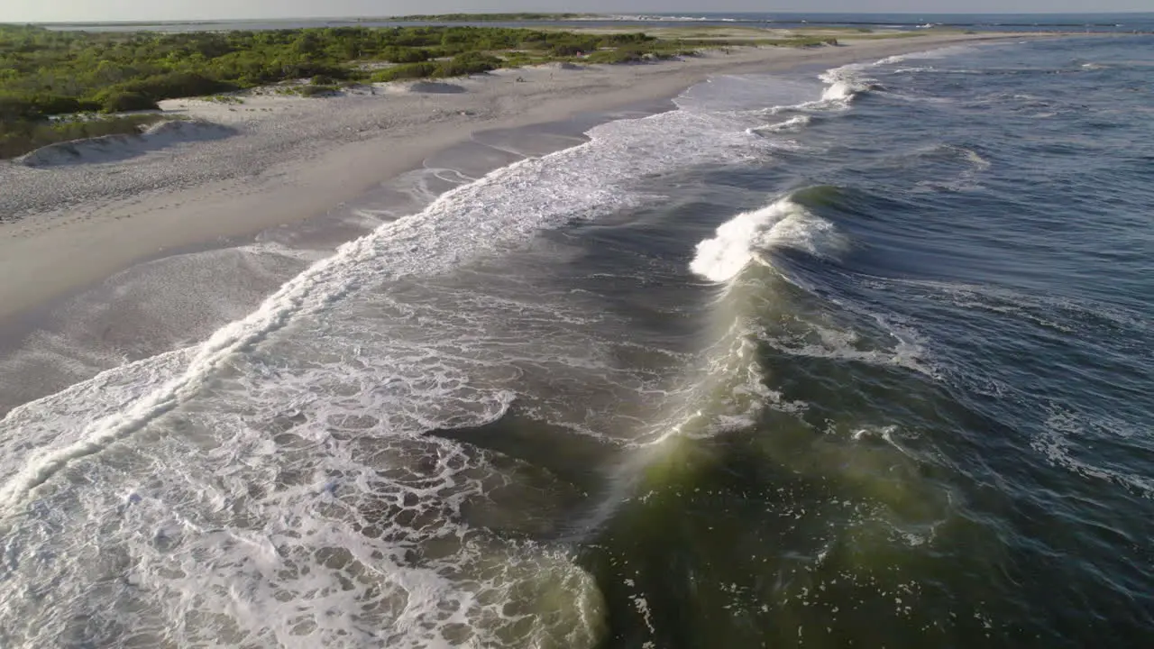 Panning drone shot over waves and surf crashing on beach only a few feet above water