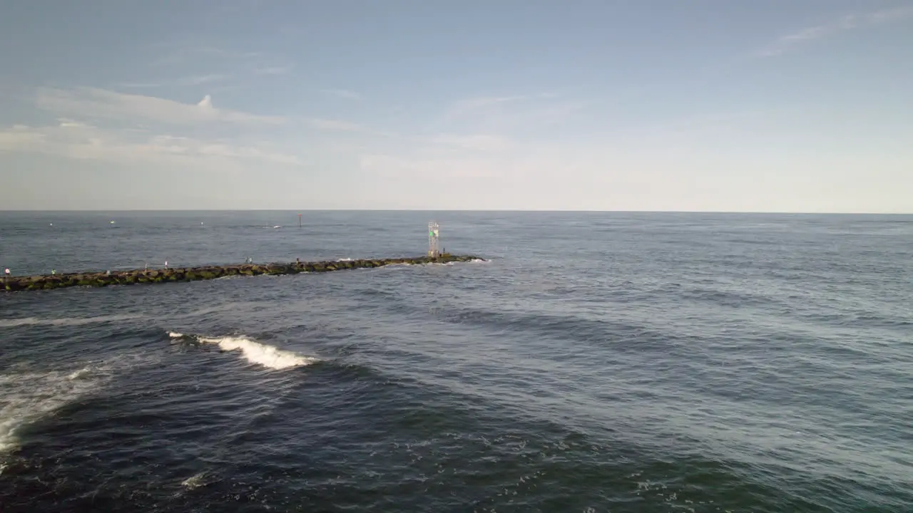 Aerial drone shot pan around light house bouy on rock jetty as man fishes with heavy lens flare