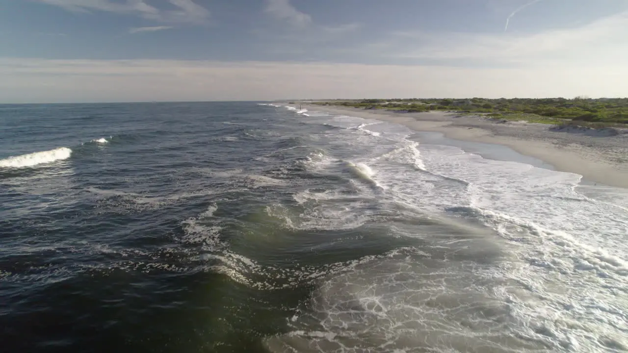 Fast drone shot moving down surf of beach over waves very near water close up