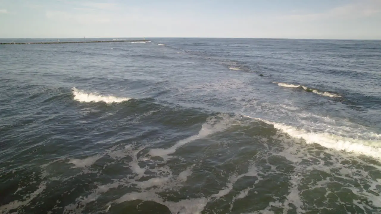 Beach drone aerial shot moving along rocks towards jetty and light house tower marking boat channel