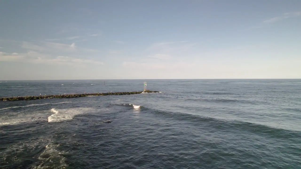 FAST Beach drone aerial shot moving along rocks towards jetty and light house tower marking boat channel