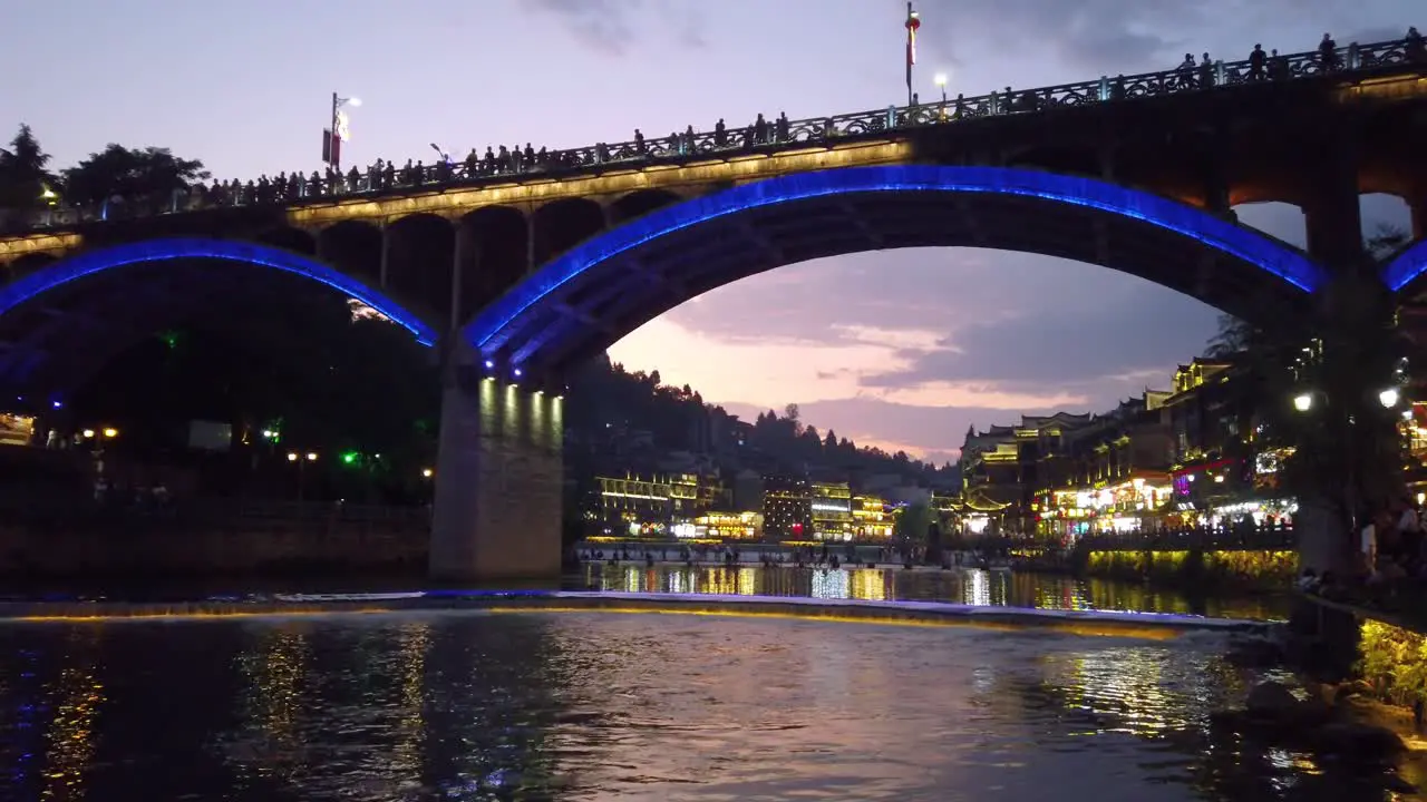 After sunset night view of the road bridge over Tuo Jiang river and wooden houses in ancient old town of Fenghuang known as Phoenix