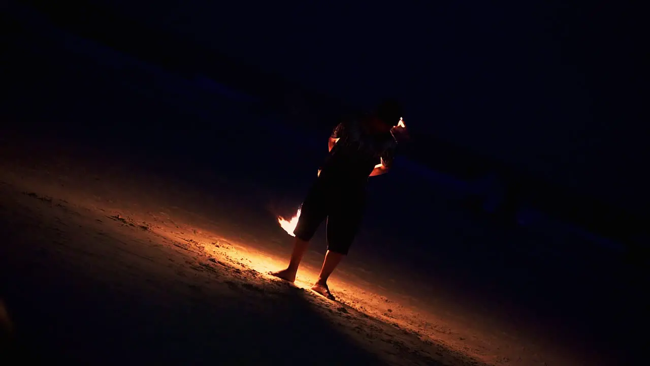 Skillful performer spinning flaming staff at night fire show on beach