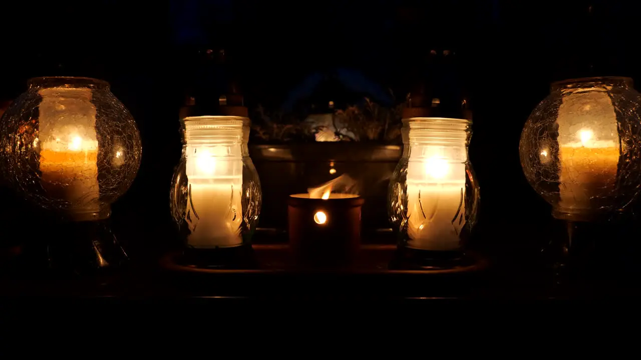 Open air grave candle framed by glass lanterns at night on a cemetery tomb