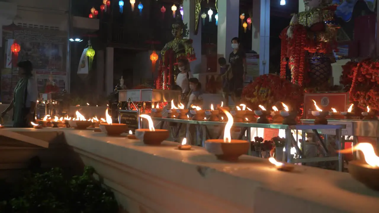 Countless traditional and holy candles burning infront of buddhist temple at night while followers leave after prayer