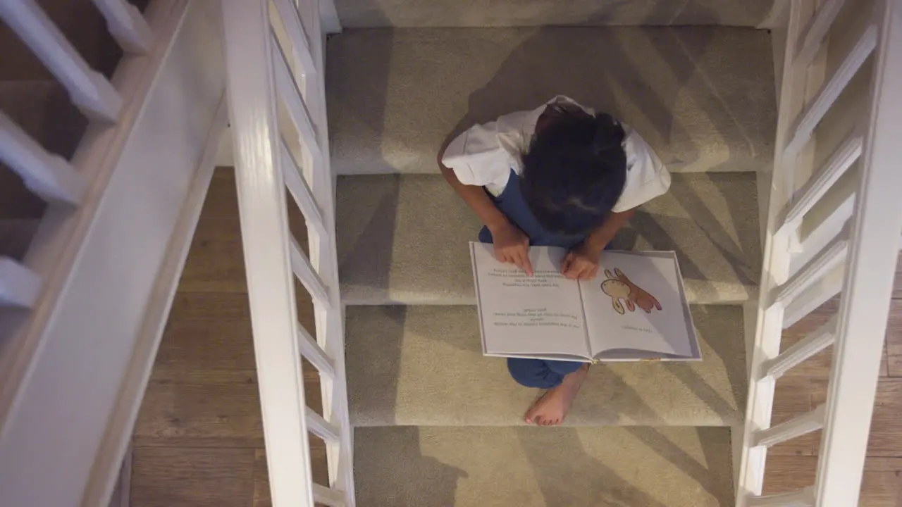 Overhead View Of Asian Girl Sitting On Stairs At Home Reading Book