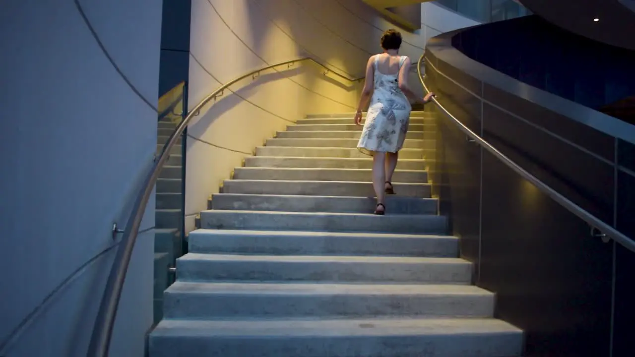 a young attractive woman in a flower and butterfly dress walks up the stairs at a leisurely pace then speeds up